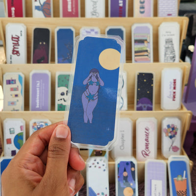 Hand holding a mermaid bookmark with a bookmark display in the background